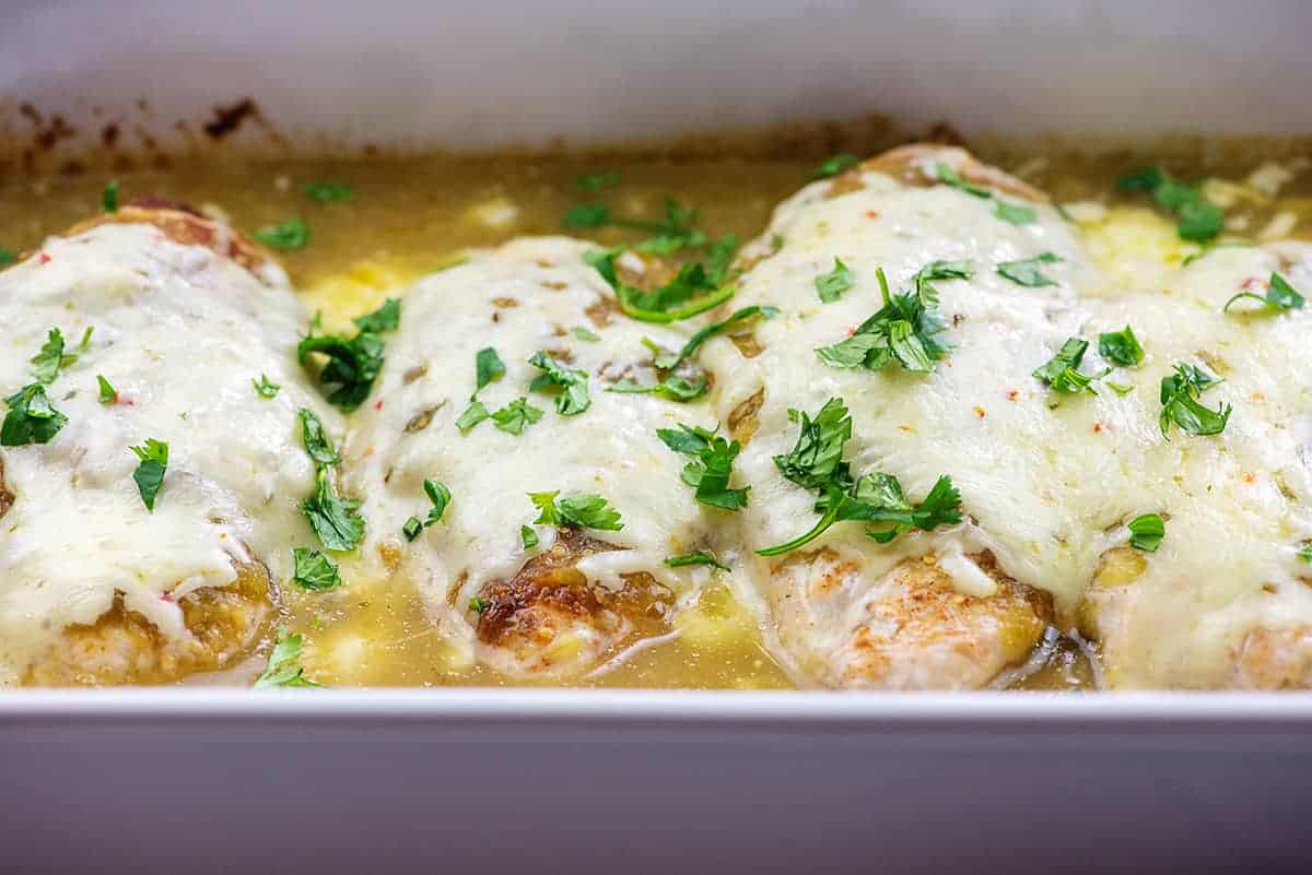 cheese topped chicken baked in salsa verde in white baking dish