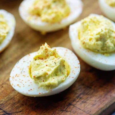 deviled eggs with paprika garnish on wooden cutting board