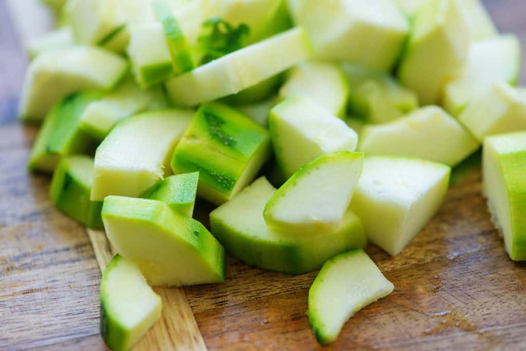 peeled and chopped zucchini on wooden cutting board