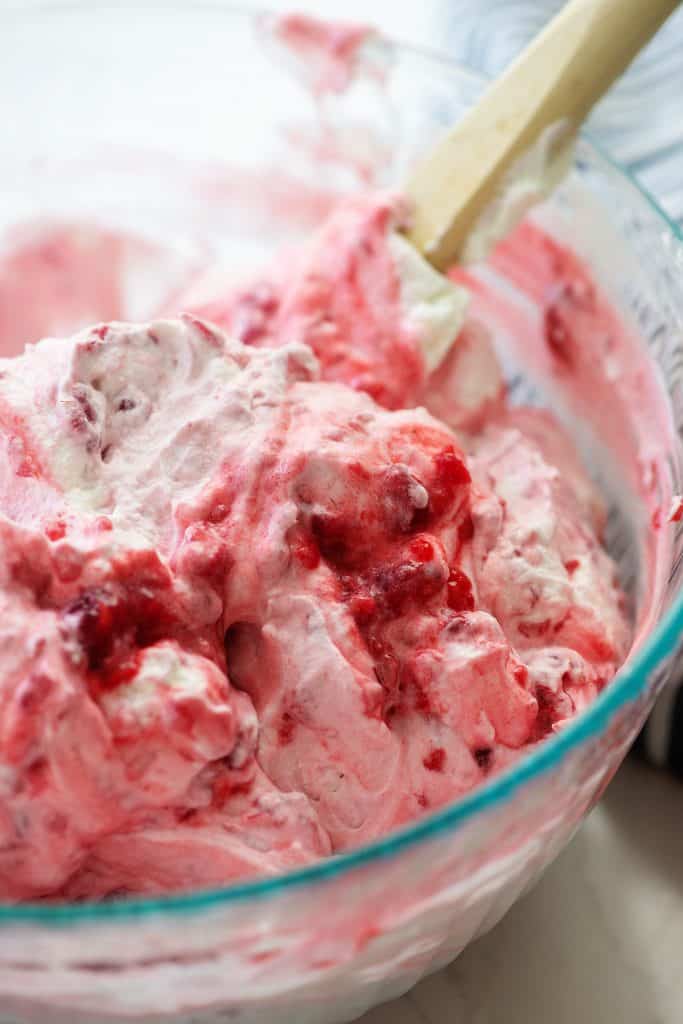 mashed raspberries folded into a bowl of whipped cream