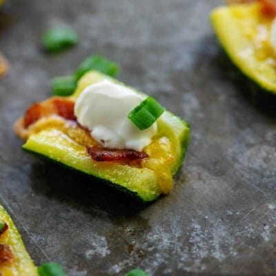 zucchini slices topped with cheddar, bacon, sour cream, and scallions on baking sheet