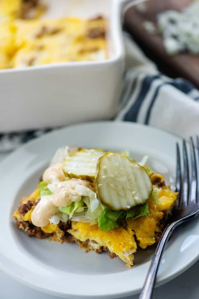 big mac casserole on white plate topped with lettuce, pickles, onion, and big mac sauce