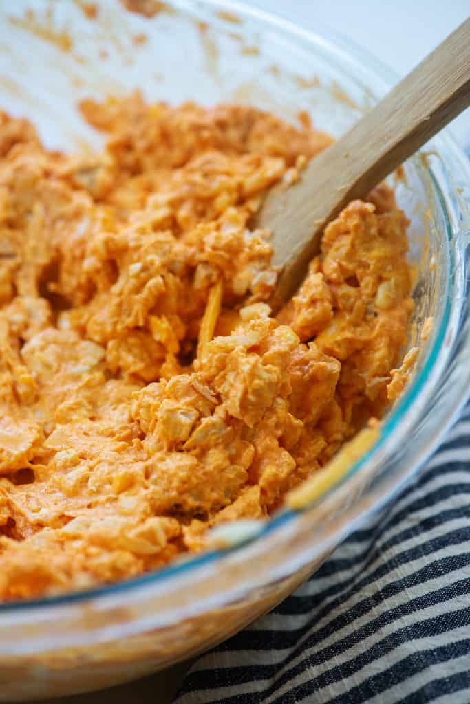 buffalo chicken dip mixture in glass bowl with wooden spoon