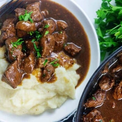 chunks of beef in gravy with mashed cauliflower on white plate