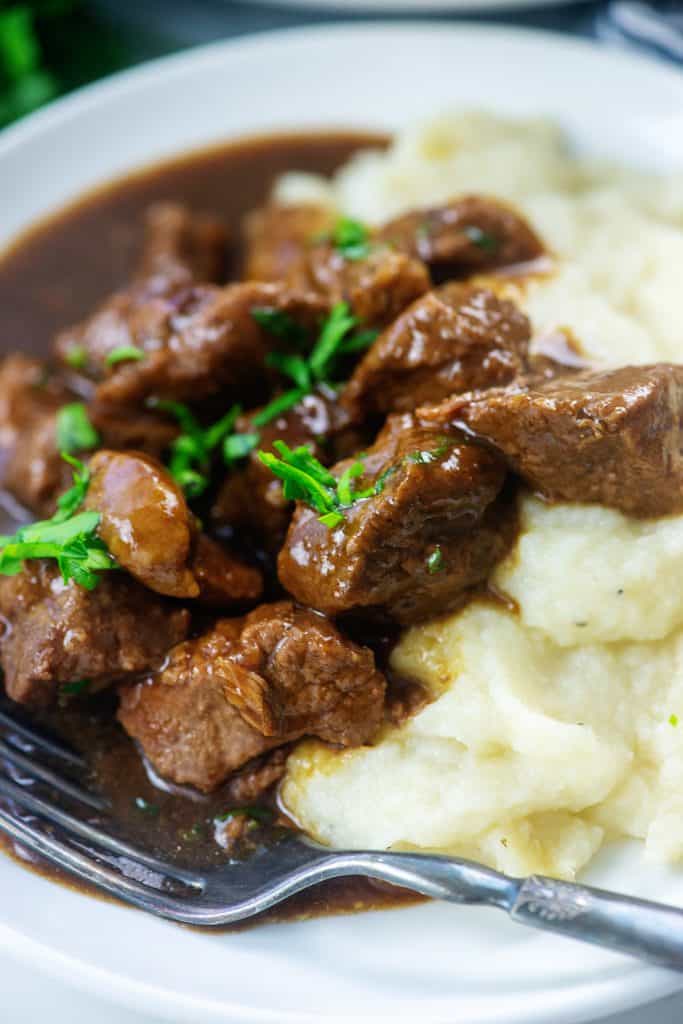 low carb beef tips on white plate with mashed cauliflower