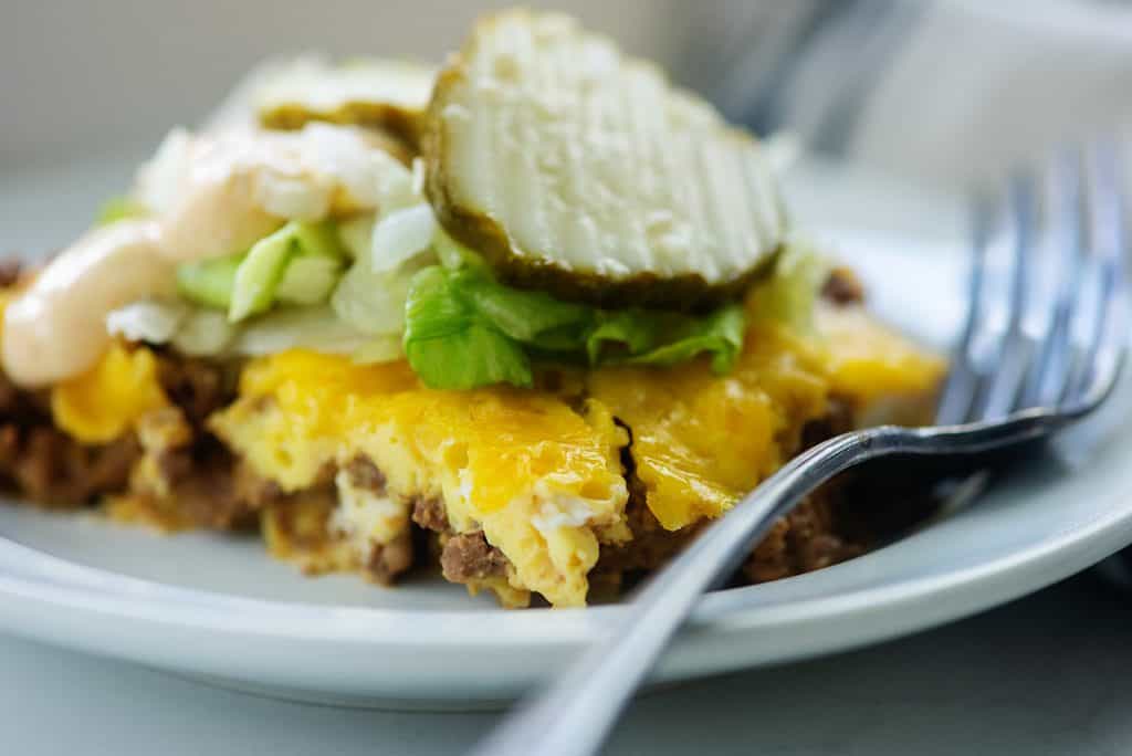 keto cheeseburger casserole topped with big mac sauce, pickles, lettuce, and onions on white plate