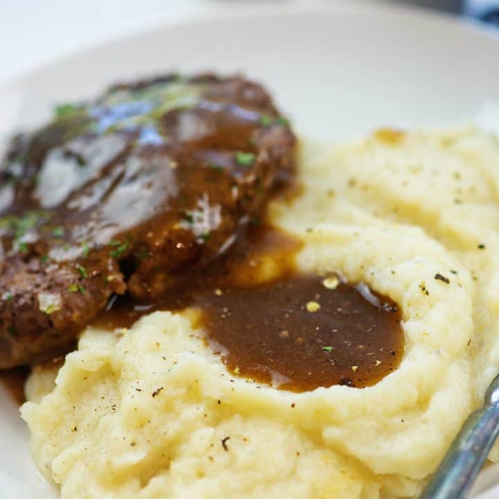 mashed cauliflower and hamburger steak topped with gravy on white plate