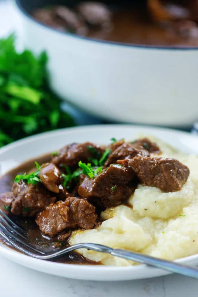 low carb beef tips on white plate with mashed cauliflower