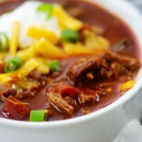 low carb chili in white bowl topped with cheese and green onions.