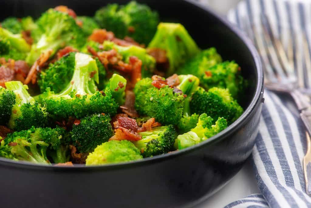 black bowl full of sauteed broccoli and fried bacon.