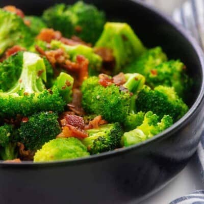black bowl full of sauteed broccoli and fried bacon.