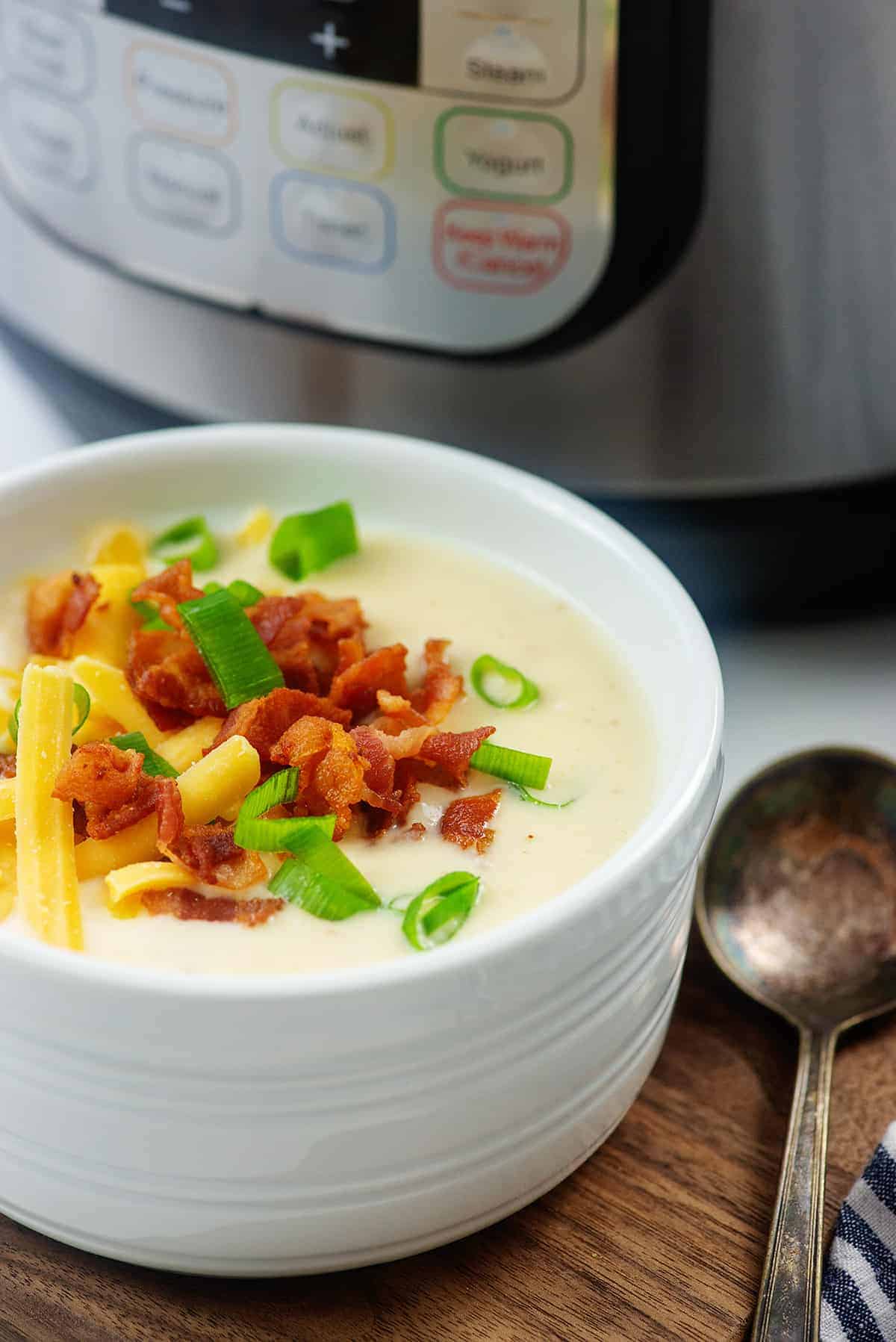 Instant Pot cauliflower soup in white bowl on wooden board.