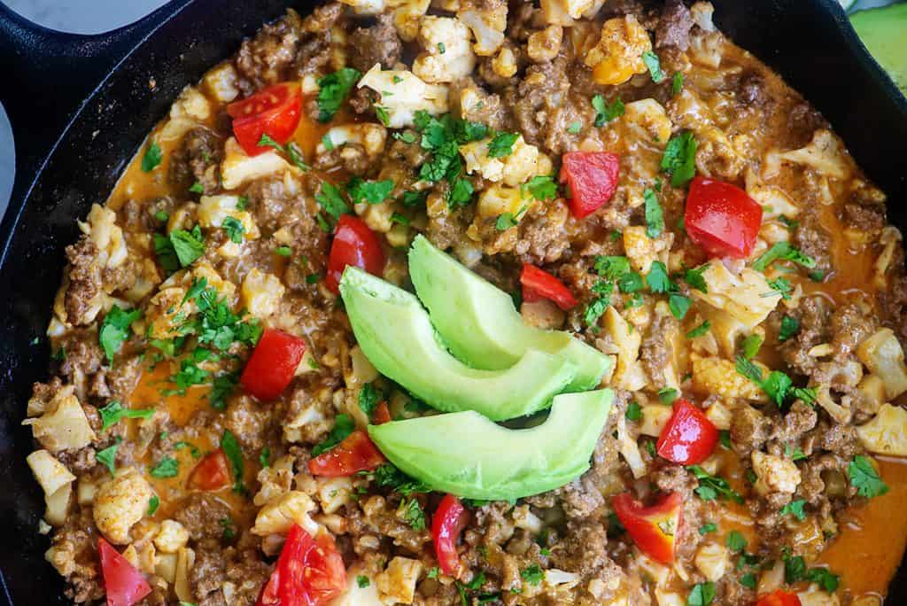 taco cauliflower recipe in cast iron skillet with avocado slices.