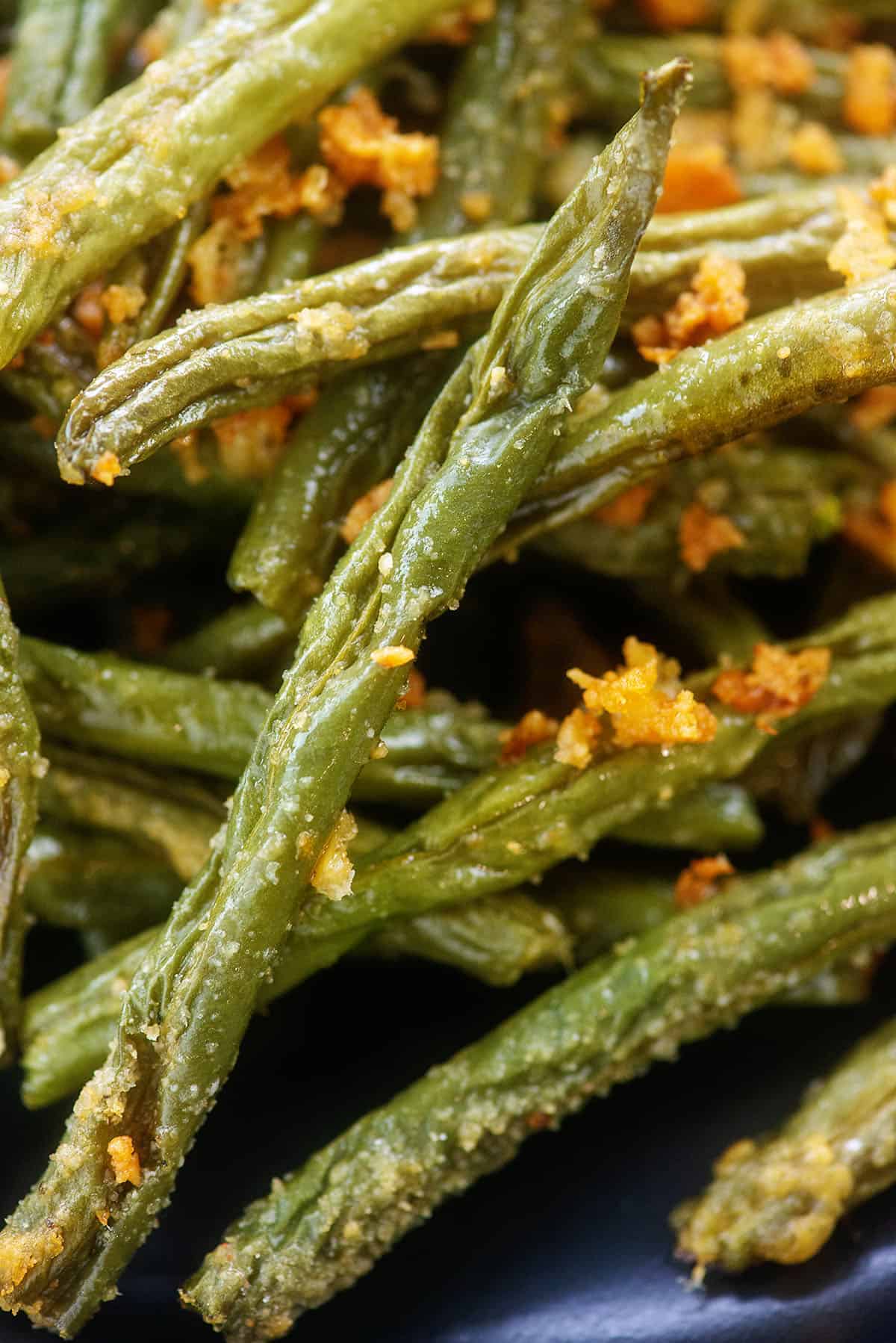 green beans coated in Parmesan on black plate.