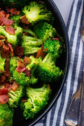 sauteed broccoli topped with bacon in black bowl.
