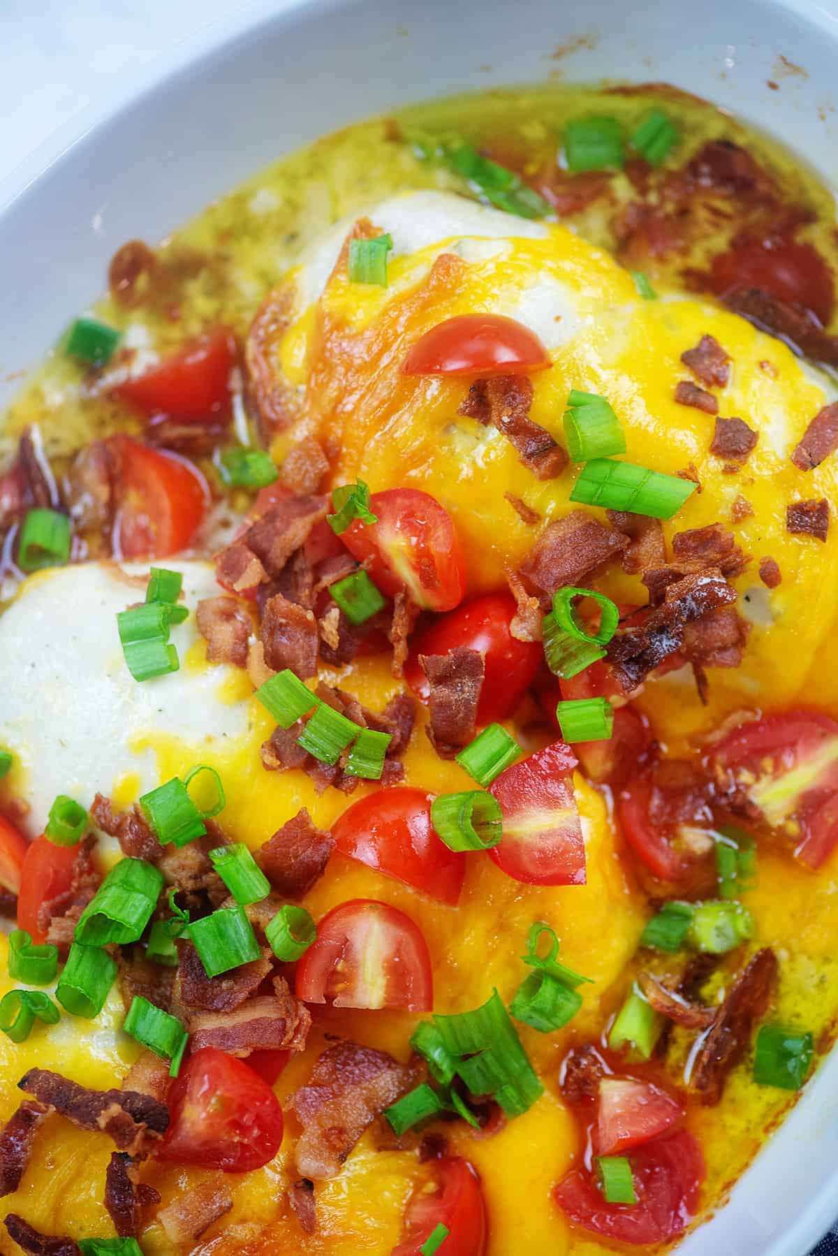 chicken in baking dish smothered with cheddar, bacon, and tomatoes.