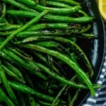 charred green beans on black plate with lemon.