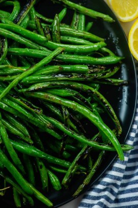 charred green beans on black plate with lemon.