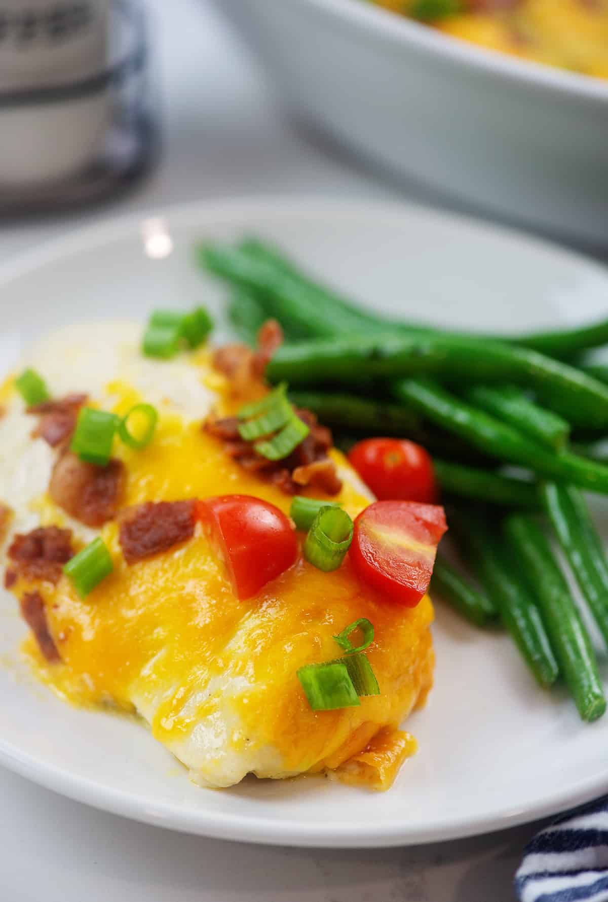 piece of chicken topped with cheddar, bacon, and tomatoes on white plate. 