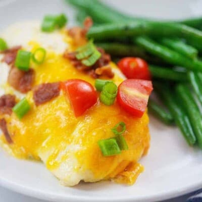 chicken breast topped with cheese and bacon on plate with green beans.