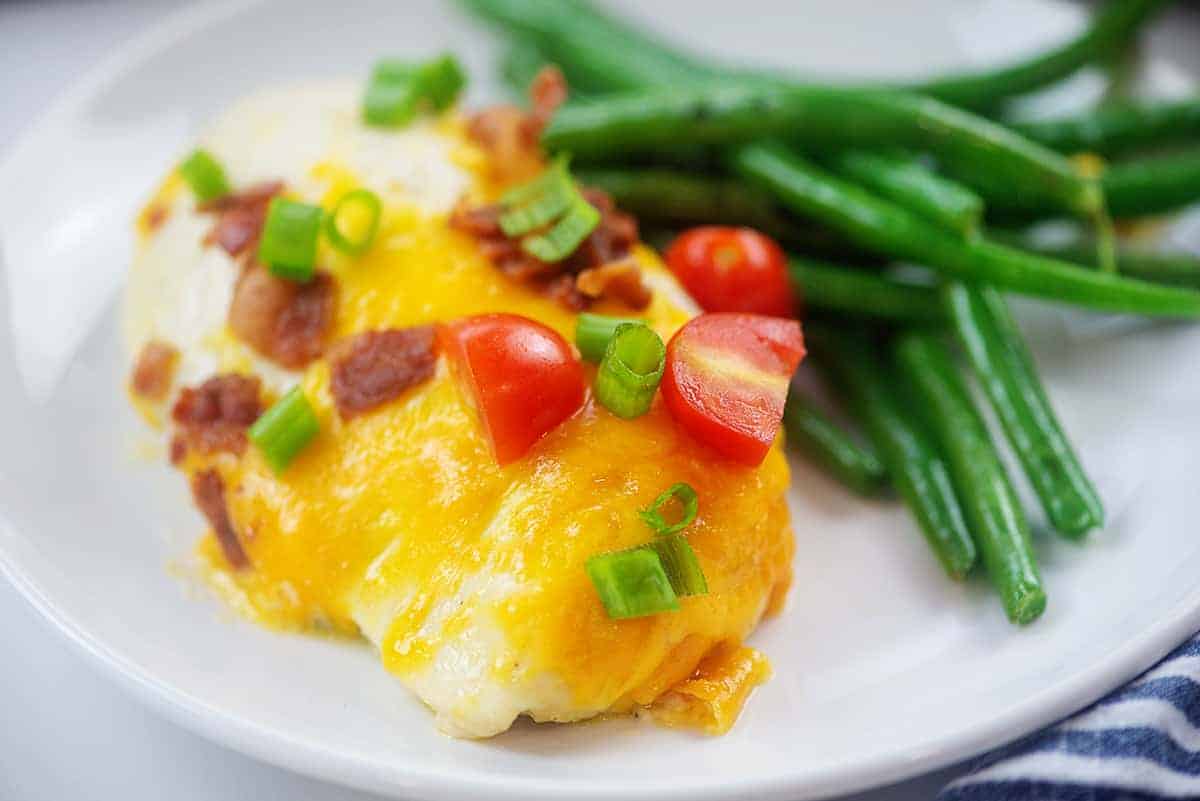 chicken breast topped with cheese and bacon on plate with green beans.