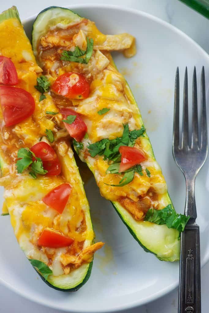 zucchini boats filled with chicken enchilada mixture on white plate.