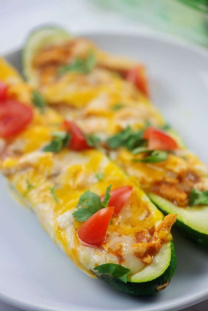 two zucchini boats on white plate topped with tomato and cilantro.