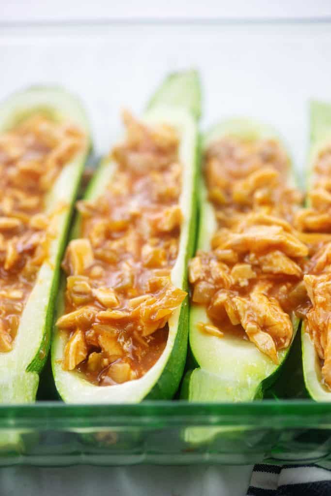 zucchini boats filled with chicken enchilada mixture in glass dish.