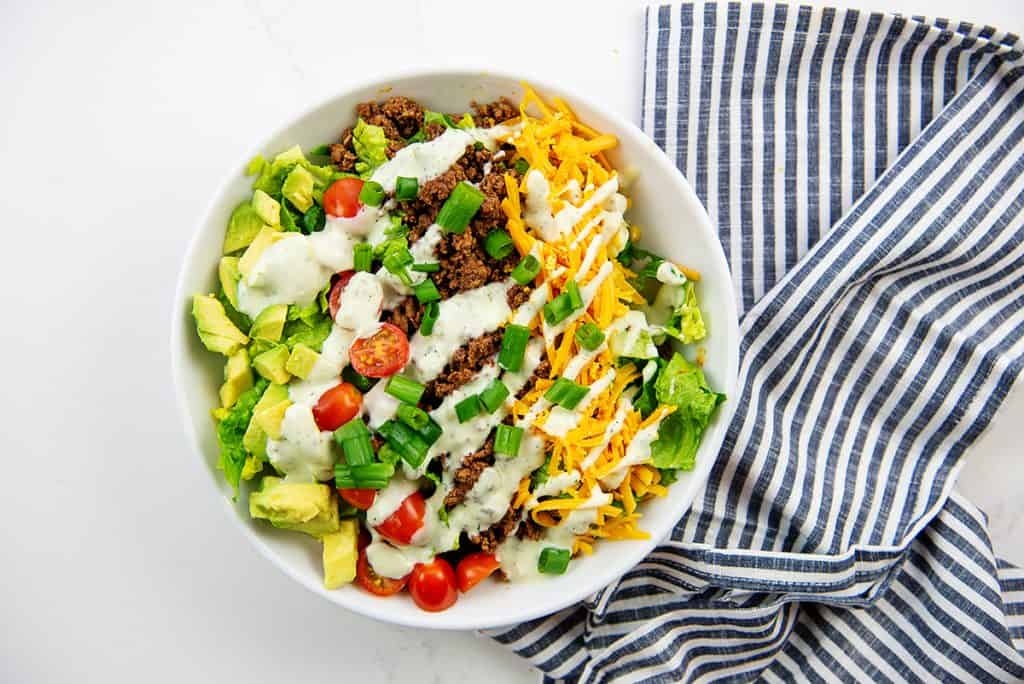 overhead view of keto taco salad in white bowl with blue napkin