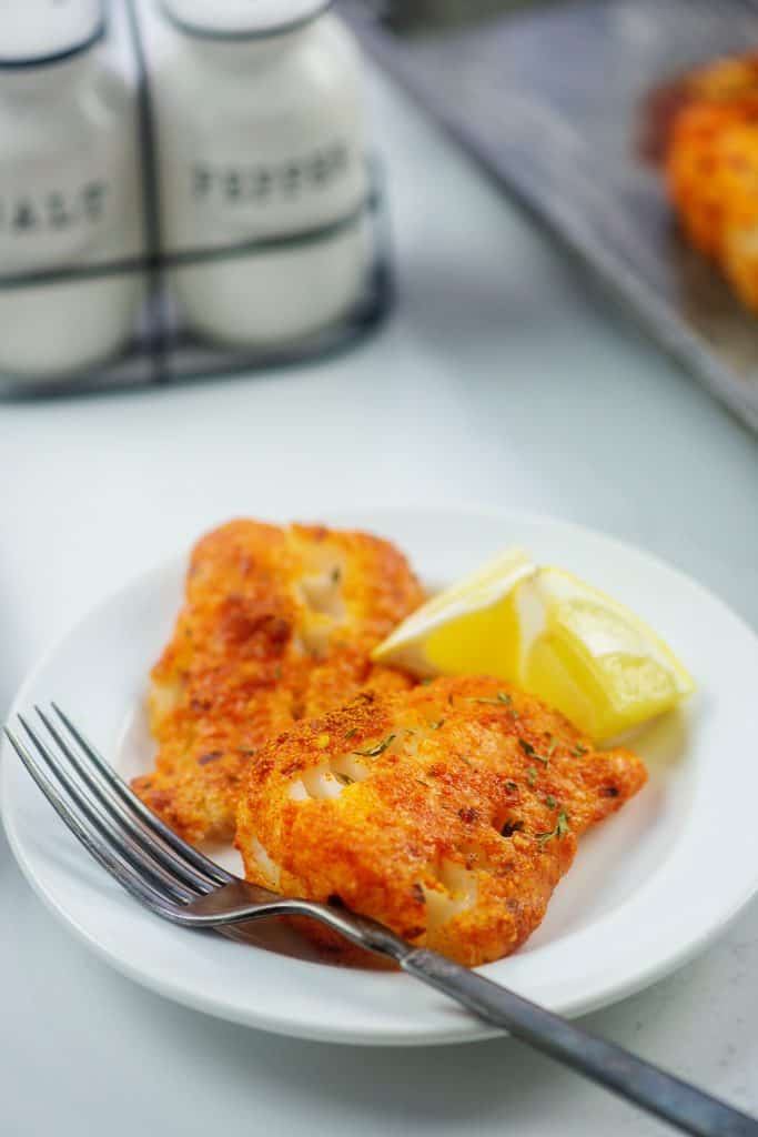 keto baked cod recipe on white plate with lemon wedges.