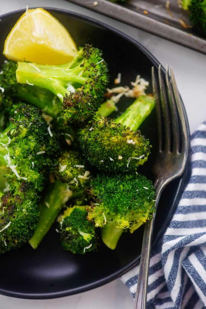 overhead view of roasted broccoli on black plate.