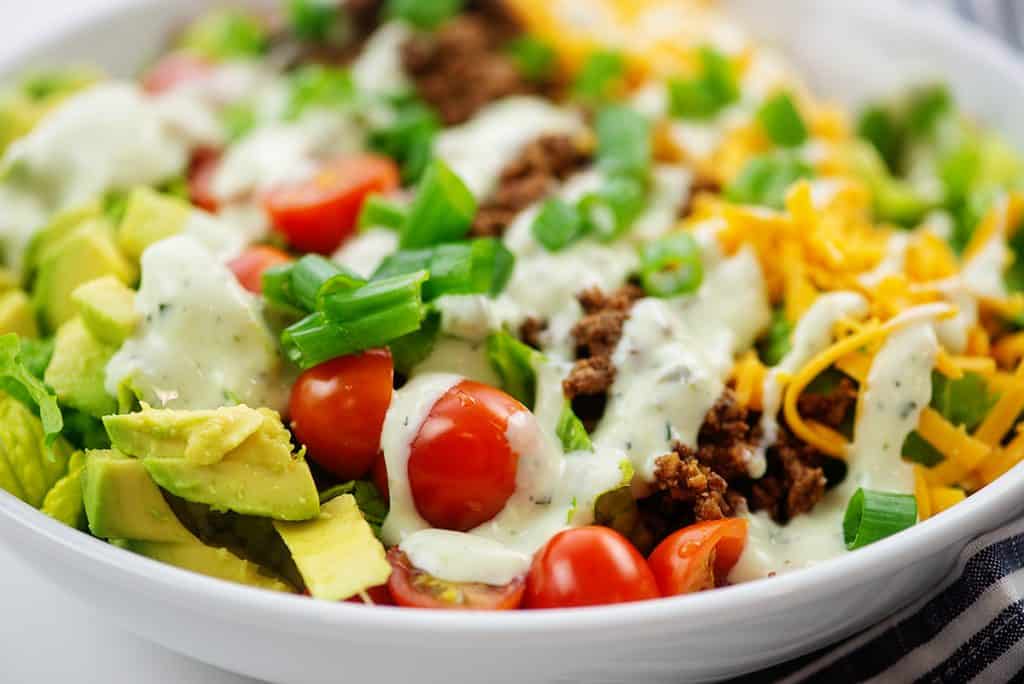 taco salad topped with avocado dressing in white salad bowl.