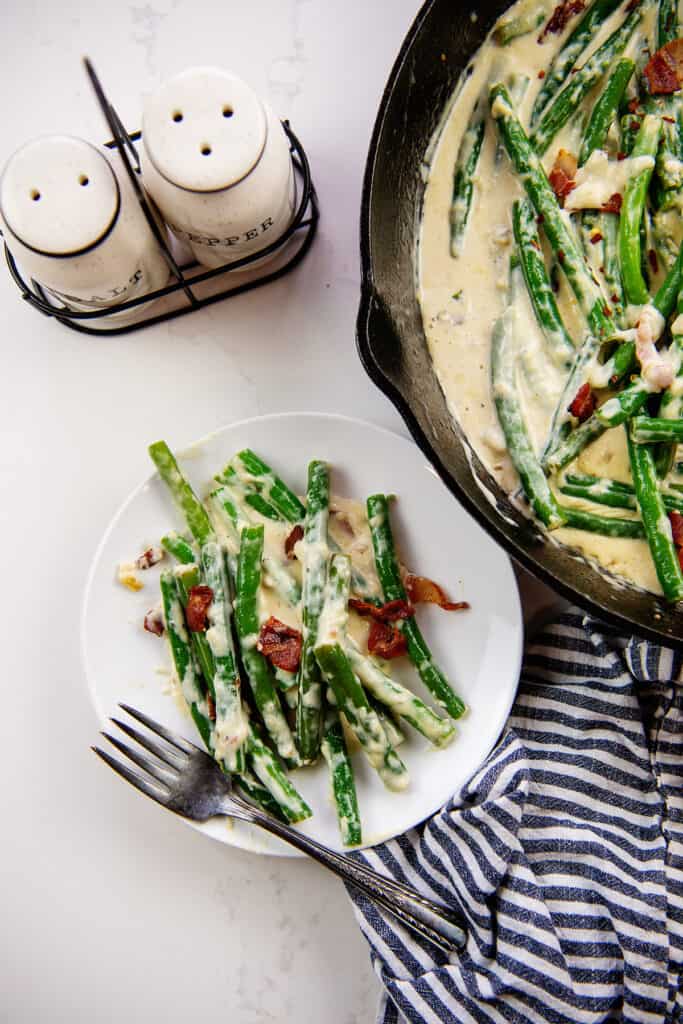 Creamy parmesan green beans on white plate next to skillet.