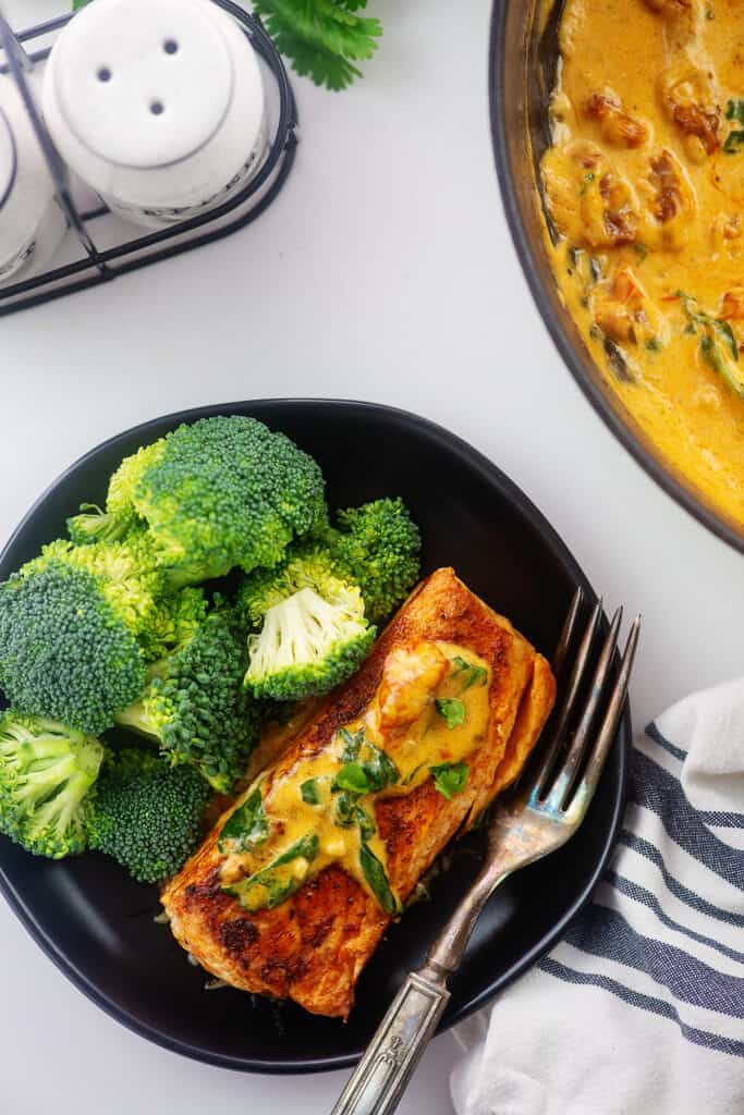 overhead view of creamy Tuscan salmon recipe on black plate with broccoli.