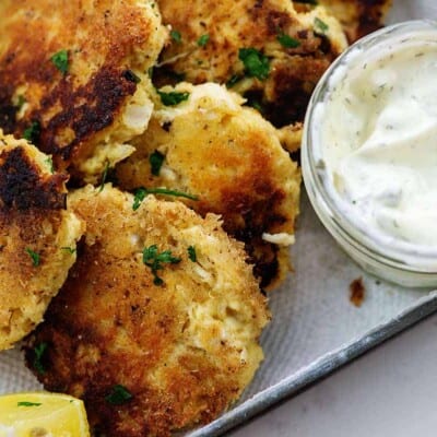 overhead view of piled up crab cakes next to tartar sauce.