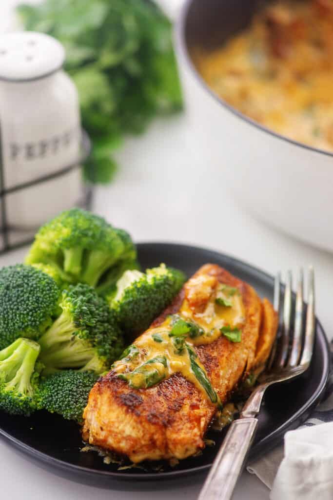 tuscan salmon recipe on black plate next to broccoli.