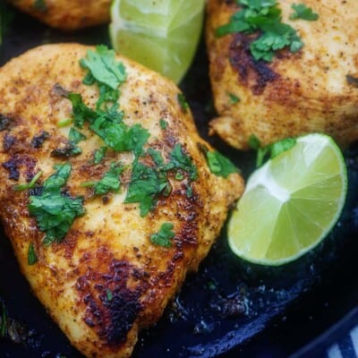 chicken breasts in black skillet with cilantro and lime.