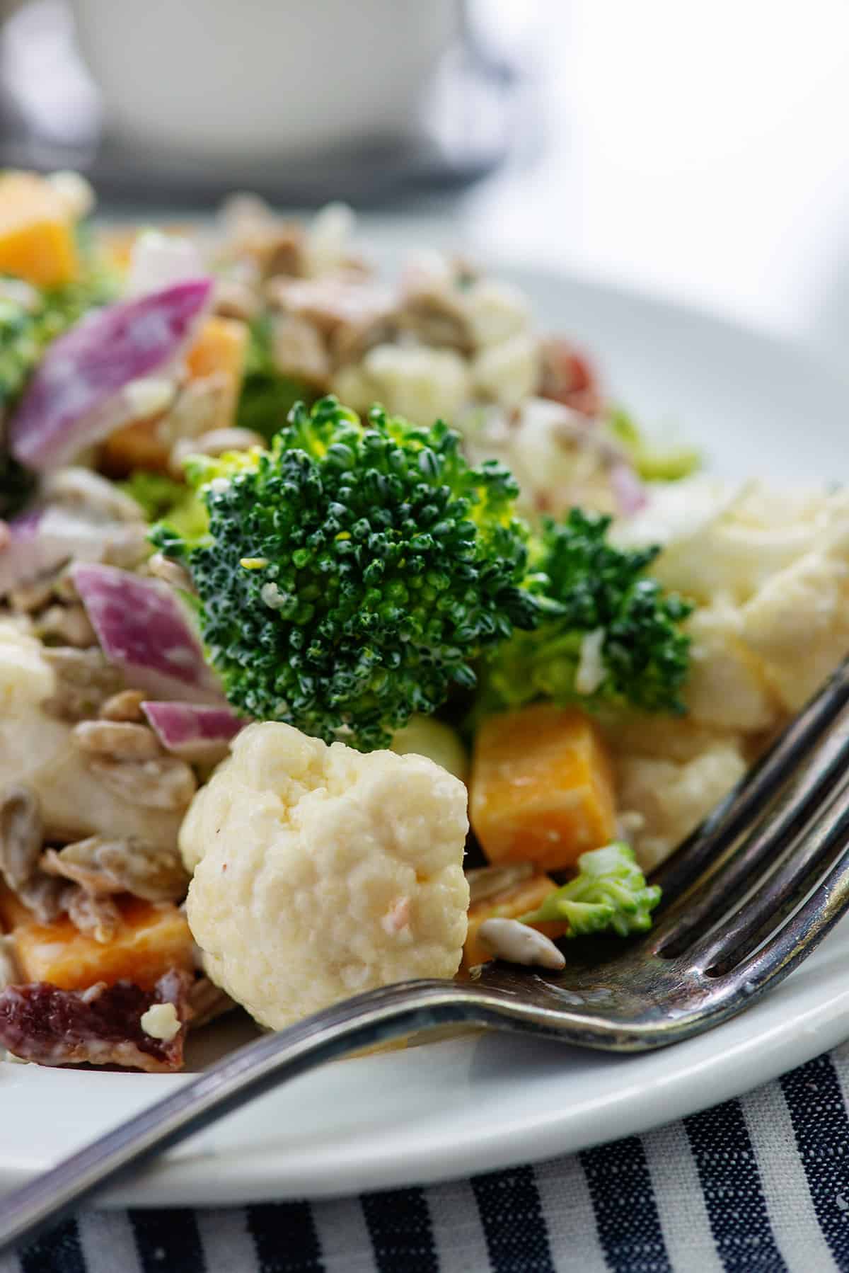 cauliflower broccoli salad on white plate with vintage fork.