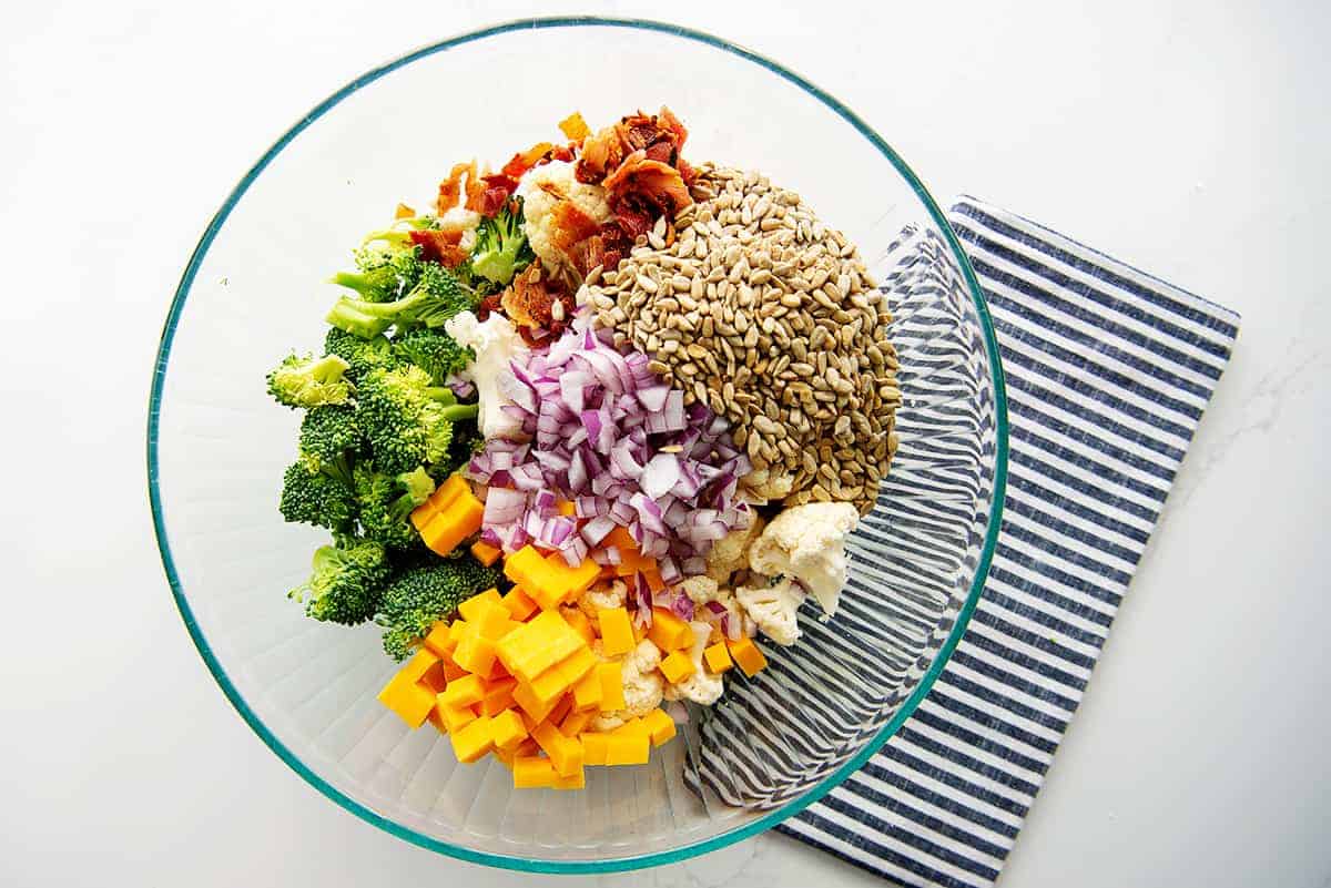 overhead view of broccoli salad ingredients in glass bowl.