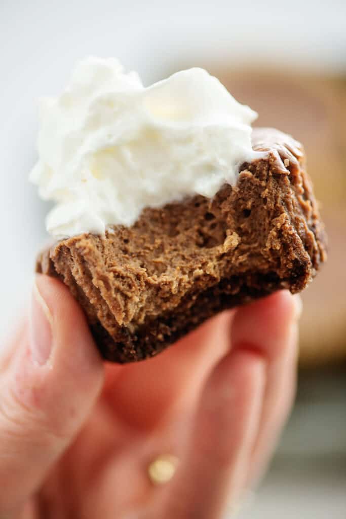 woman holding a mini chocolate cheesecake with a bite taken out.