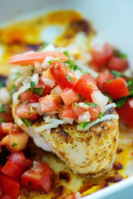 baked chicken breasts topped with salsa fresca in white baking dish.