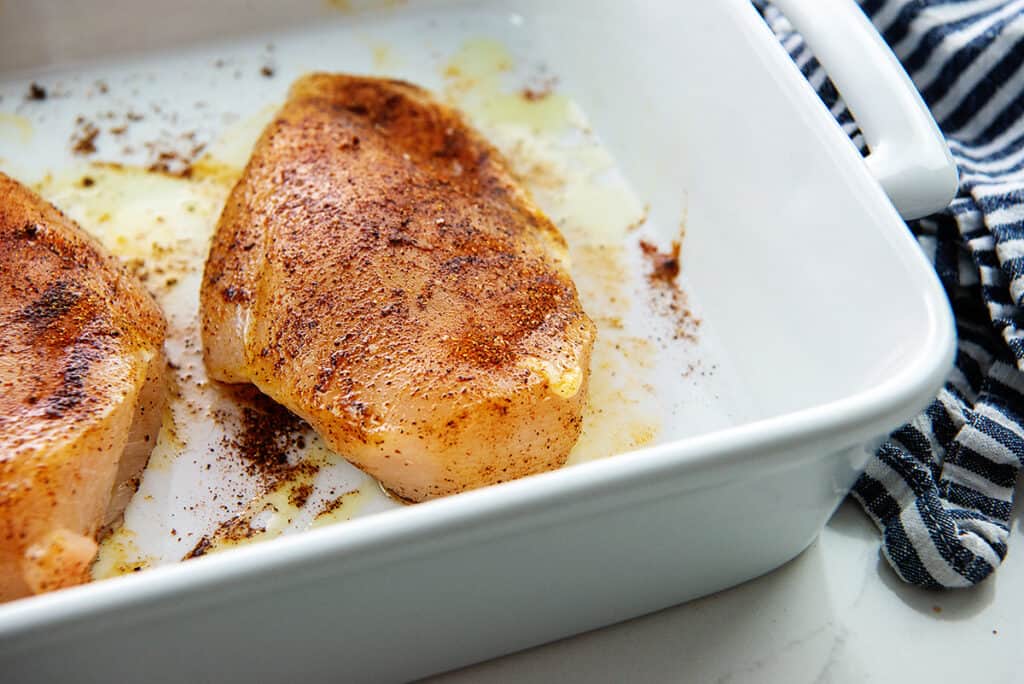 seasoned chicken breasts in white baking dish.