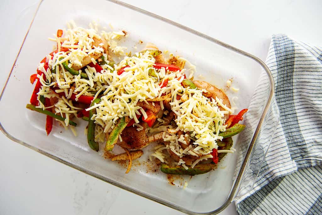 chicken in glass dish topped with vegetables and cheese.