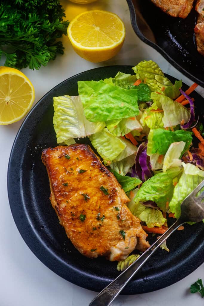 lemon garlic pork chops with salad on black dinner plate.