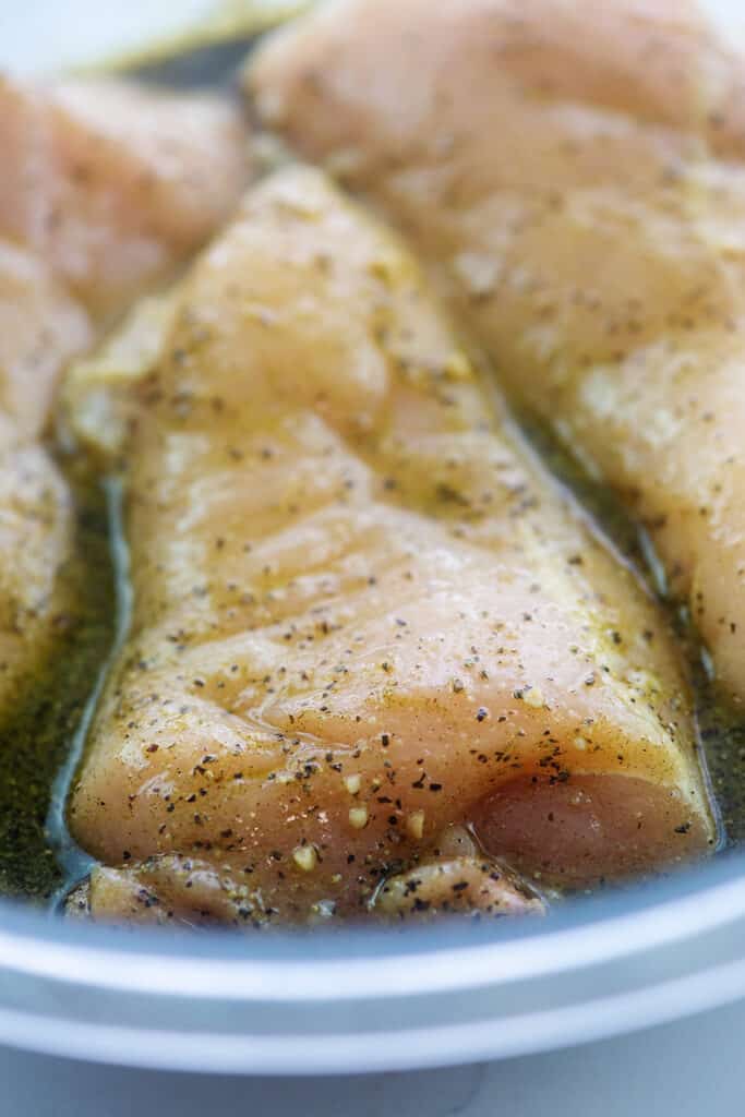 chicken breast in Greek chicken marinade in glass bowl.