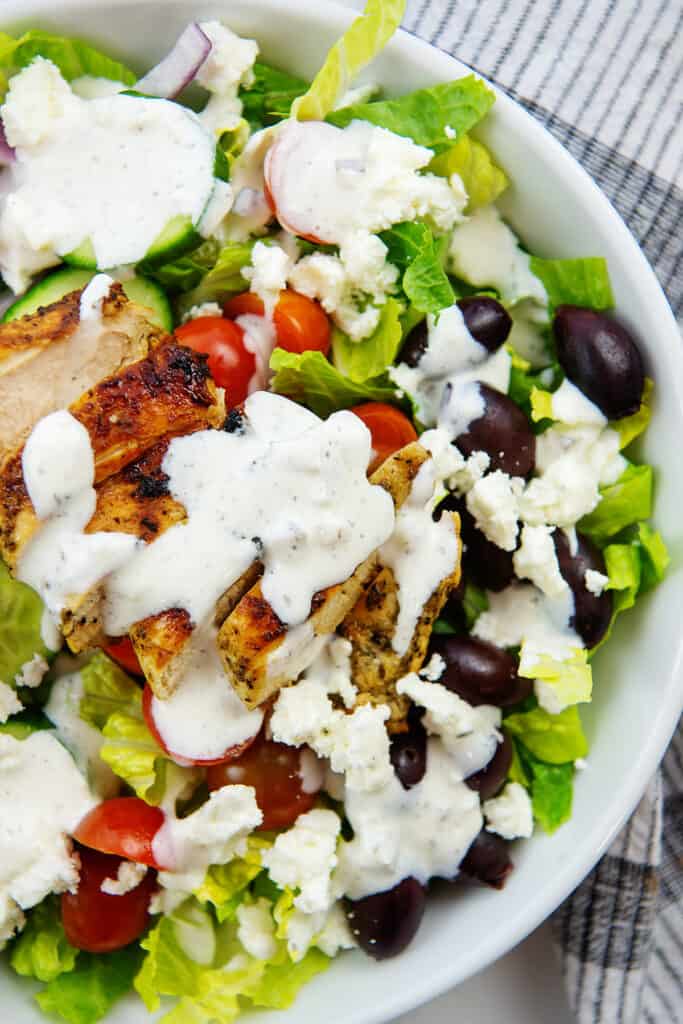 overhead view of Greek chicken salad with tzatziki dressing in white bowl.