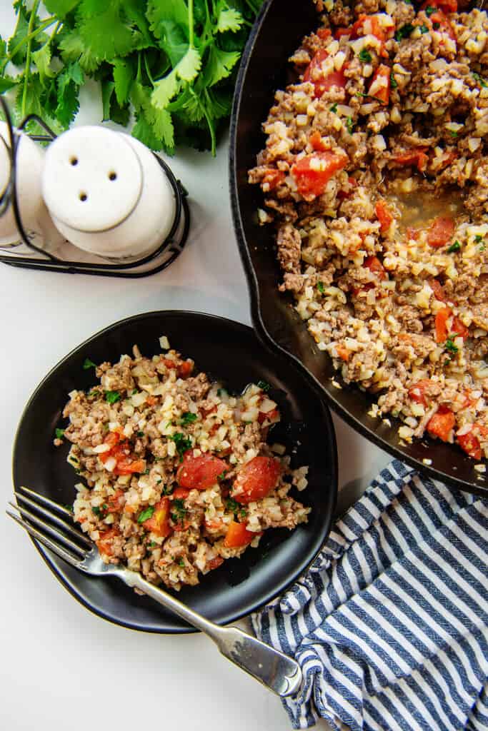 Italian cauliflower rice on black plate next to cast iron skillet.