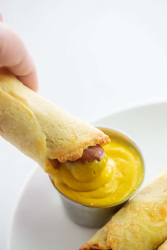 pigs in a blanket being dunked in mustard.
