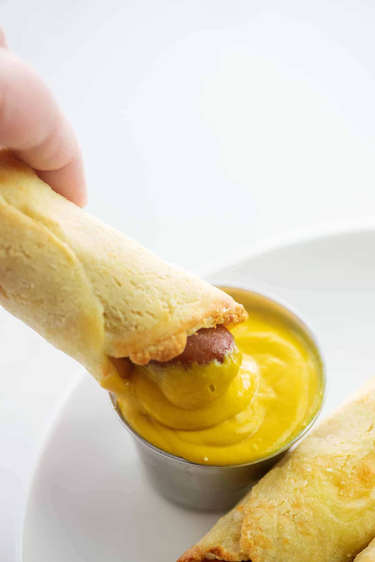 pigs in a blanket being dunked in mustard.