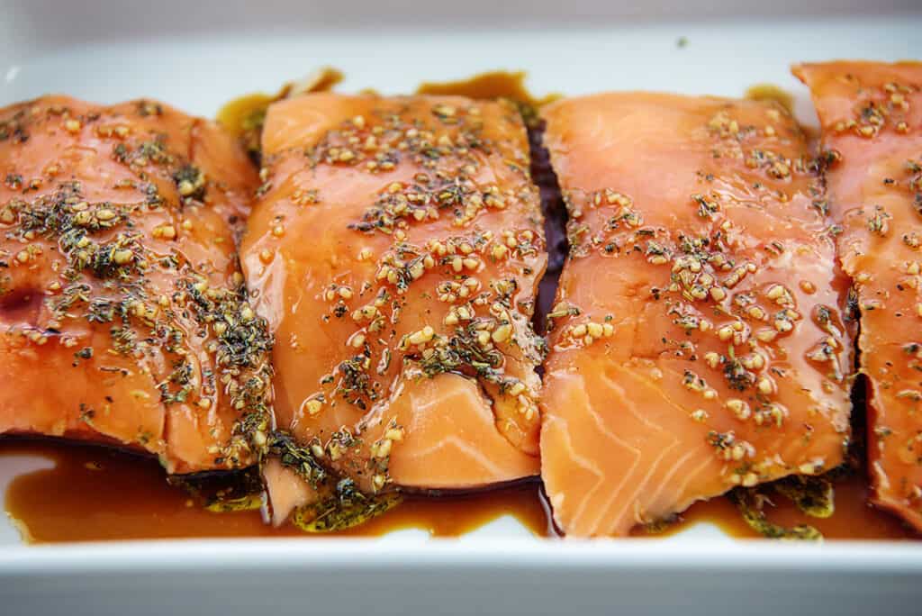 salmon in marinade in white baking dish.